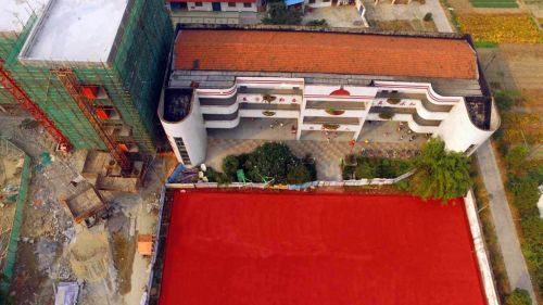 教学楼下学生们在活动，紧邻着正在建设的塑胶场地